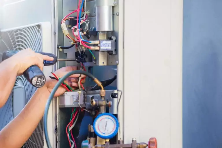 A person uses a screwdriver and tool to work on the exposed wiring and components inside an air conditioning unit during routine AC maintenance for Horizon Air.